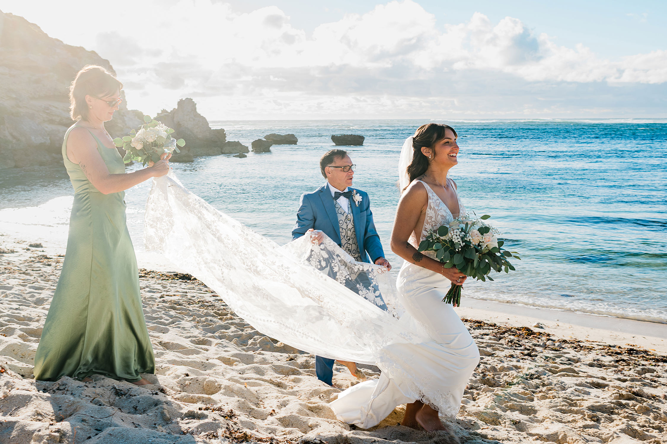 Bride smiling as her veil is held while walking across the shore during an elopement beach wedding in Margaret River at Gnarabup.