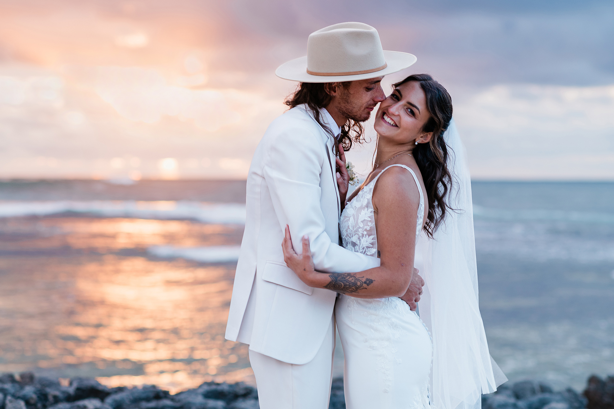 Bride and groom embracing warmly on the rocky shore during a golden hour Gnarabup Beach wedding portrait session.