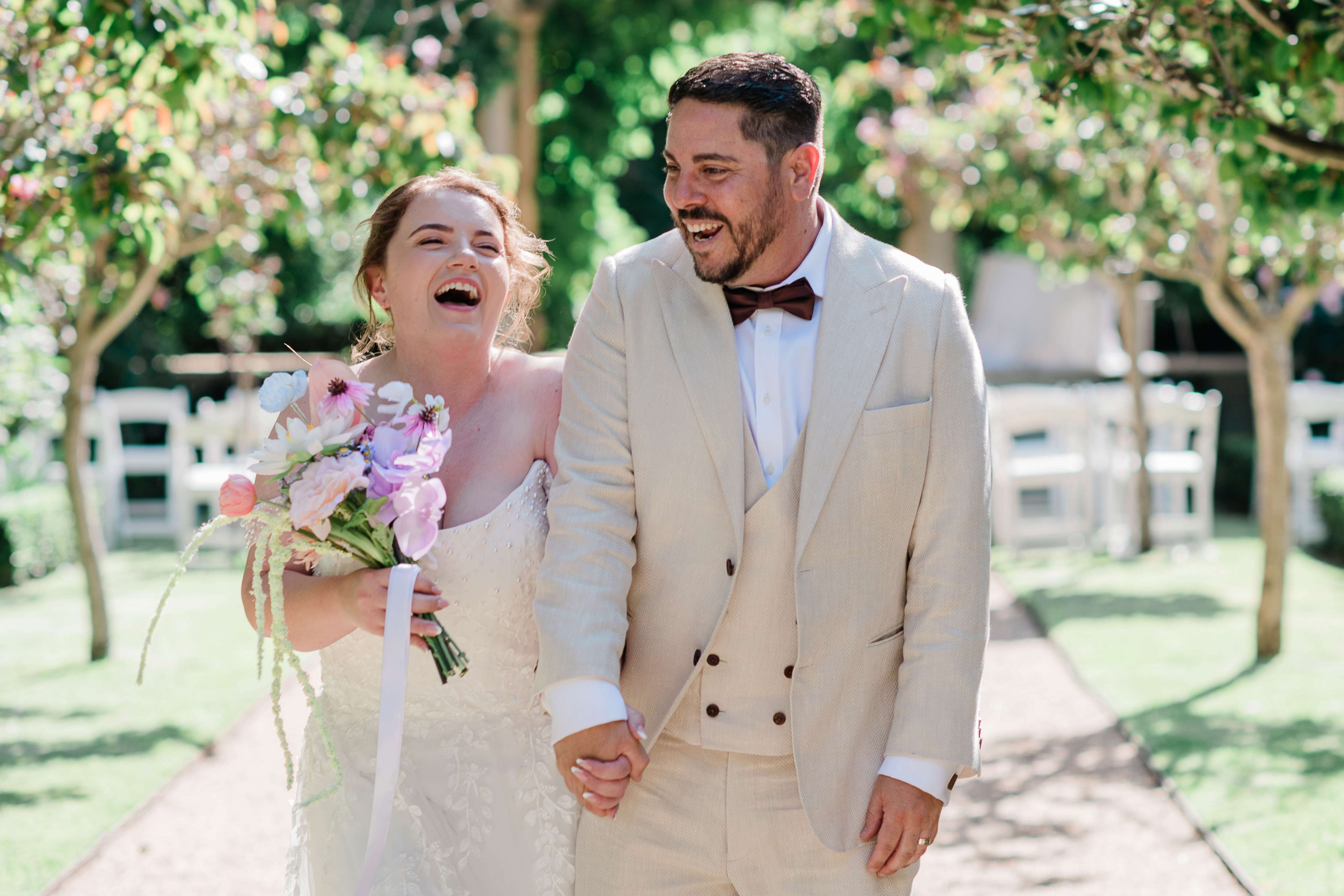 Margaret River Secret Garden wedding bride and groom laughing on garden path, bride holding pastel wildflower bouquet with trailing amaranthus