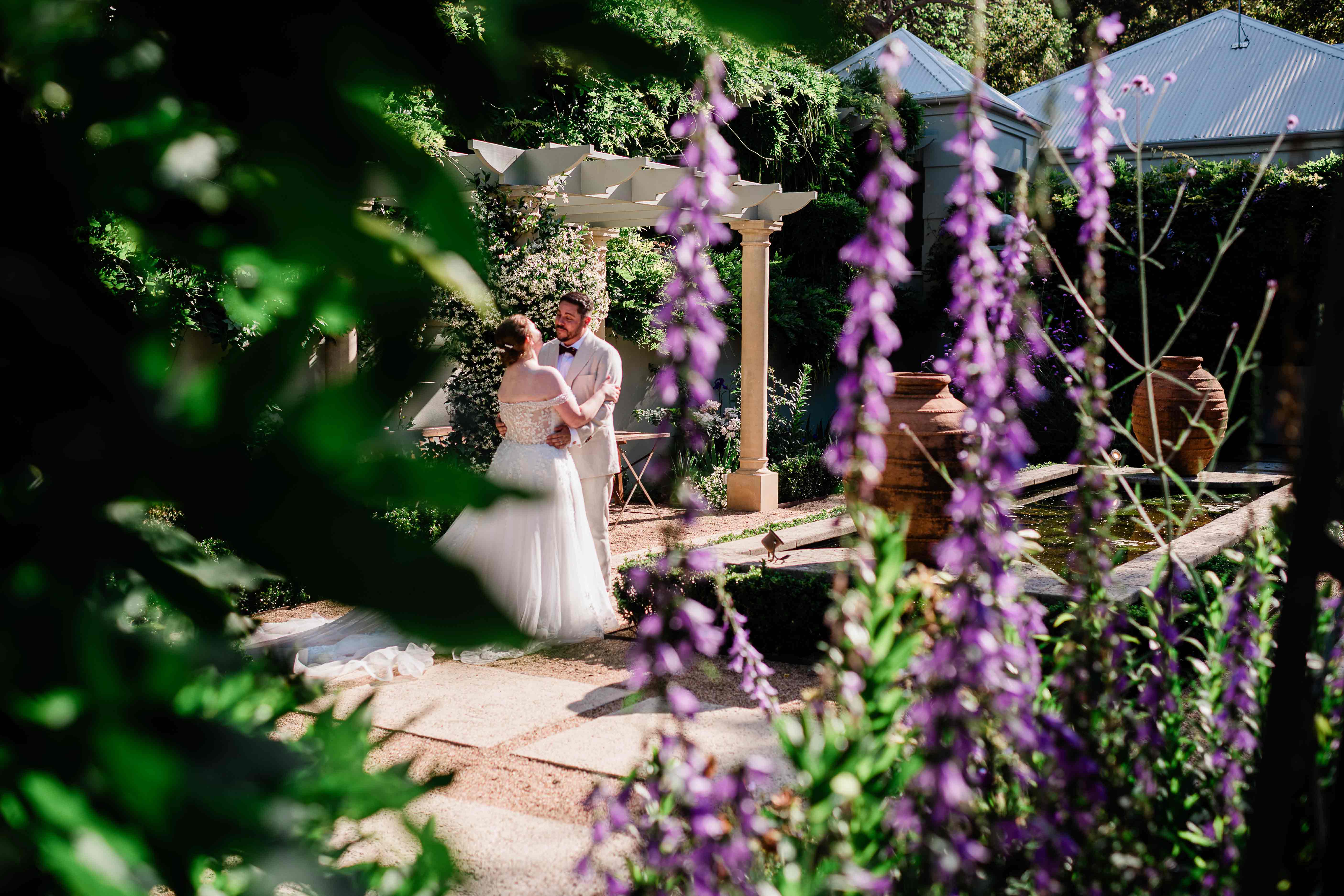 Margaret River Secret Garden wedding couple embracing beside sandstone pergola and reflection pond framed by salvia spires