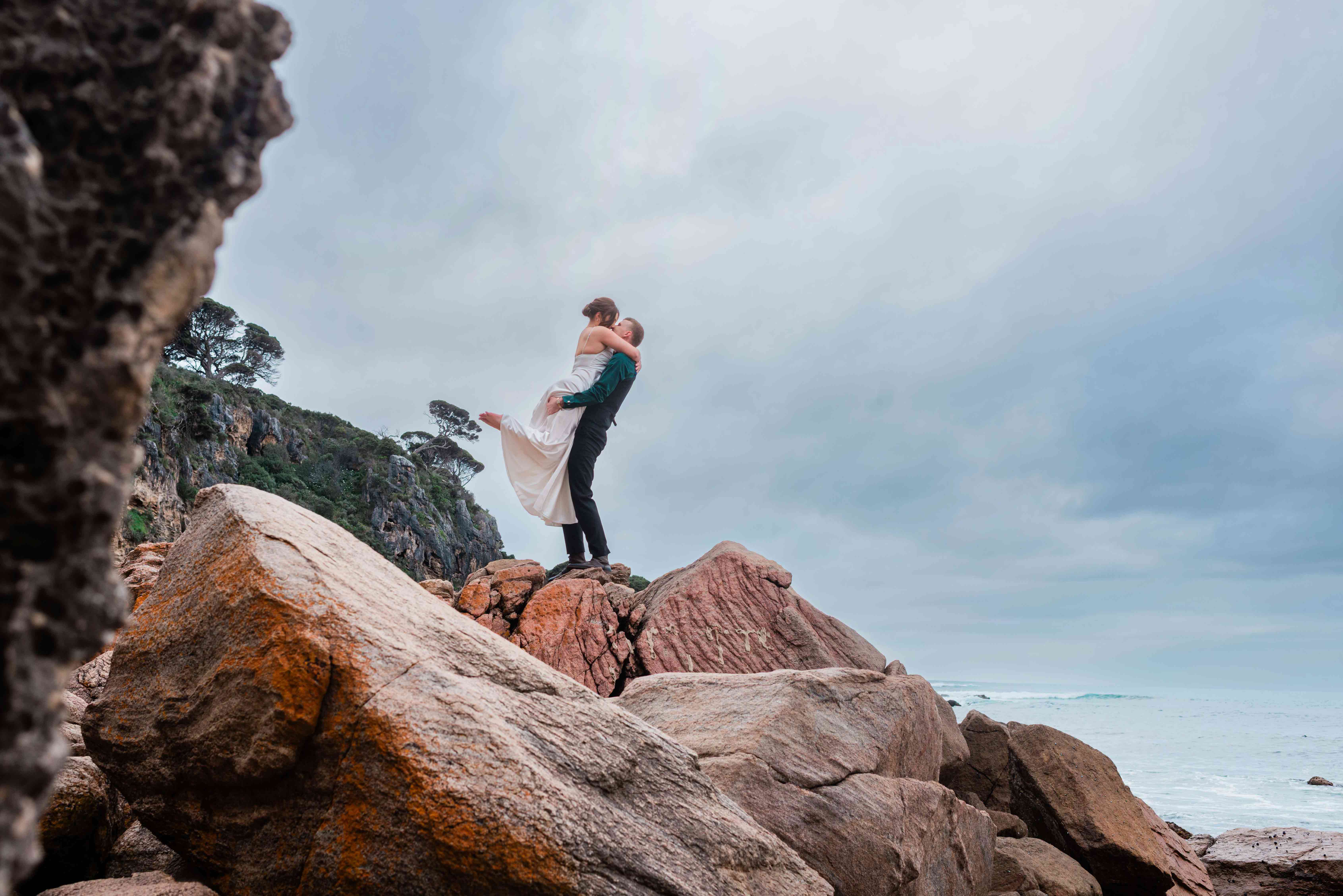 Luxury elopement Margaret River couple embracing on orange lichen rocks at Shelley Cove near Bunker Bay, photographed by John Rice