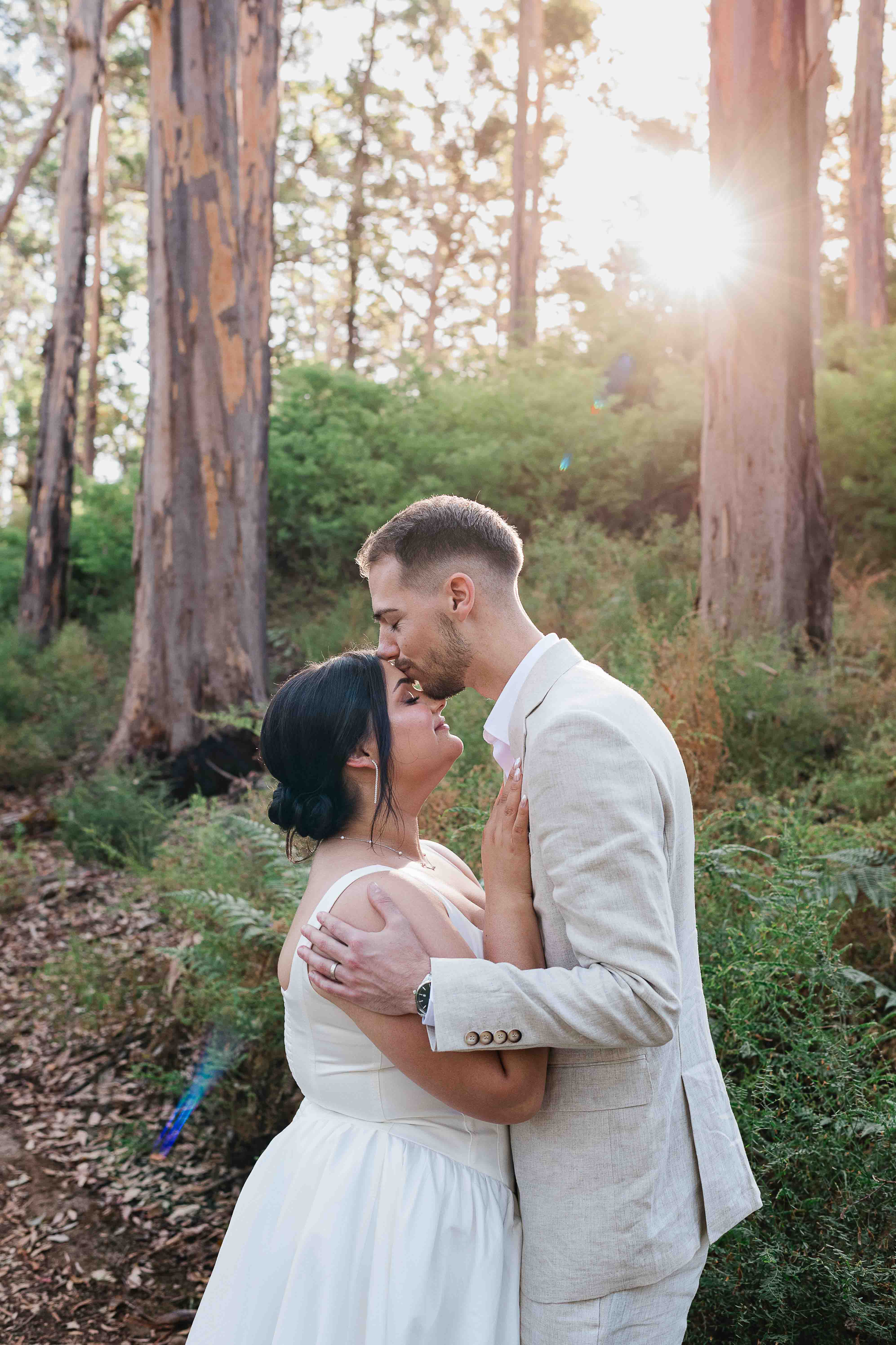 groom affectionately kisses bride on her forehead golden light through trees boranup forest