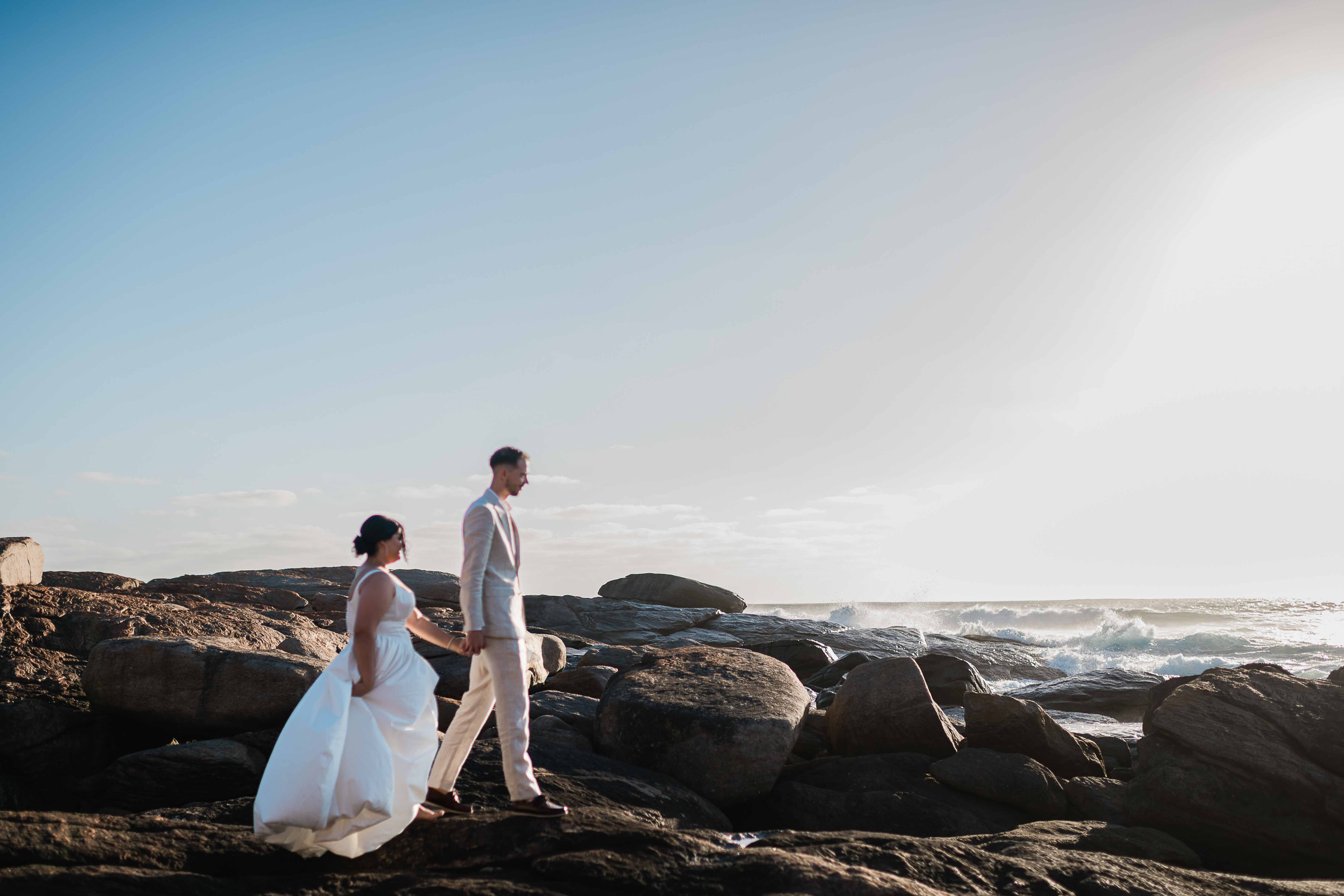 dramatic beach elopement bride groom walk holding hands towards beautiful golden hour light