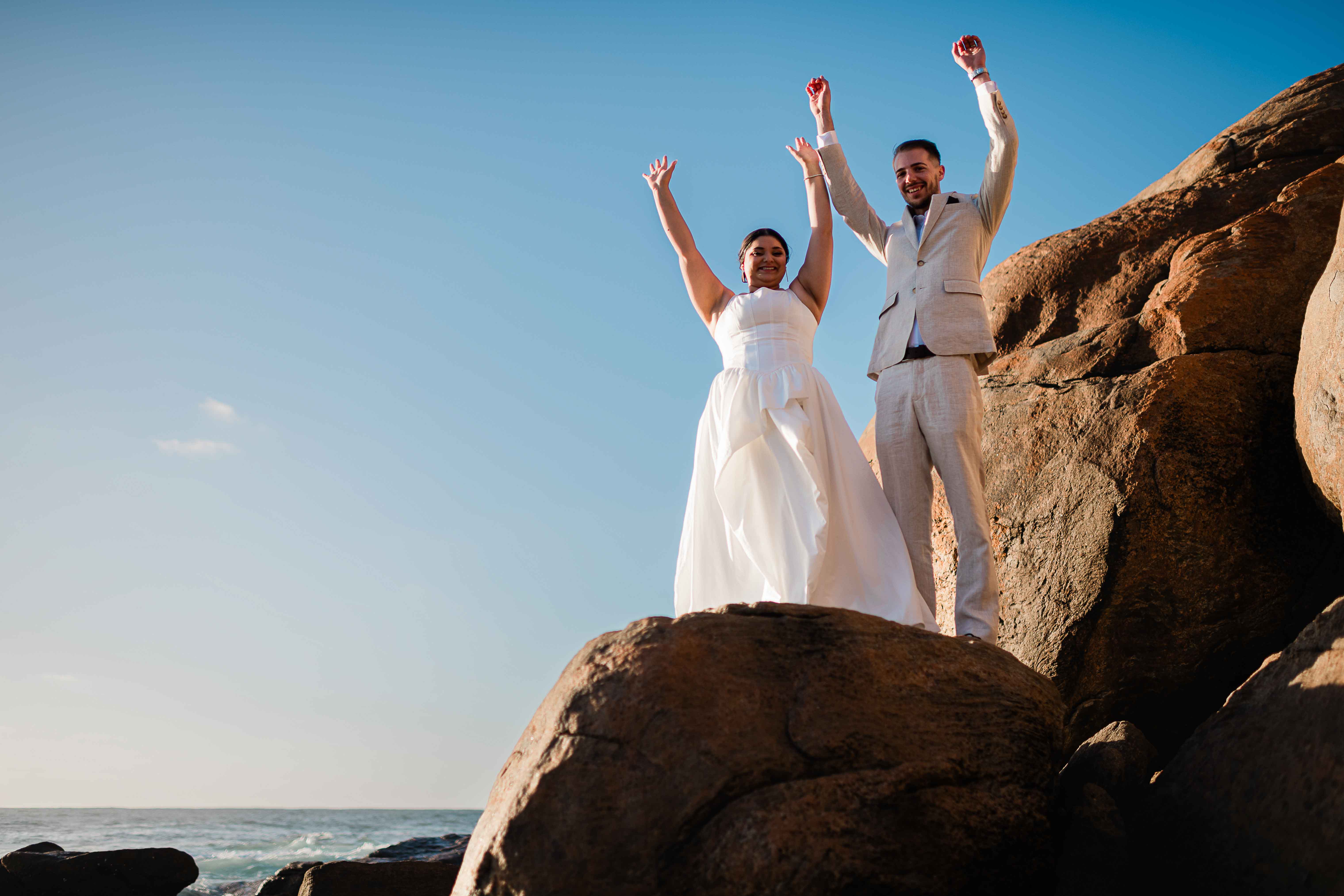 bride and groom hold their hands aloft smiling celebrating their elopement with dramatic beautiful margaret river beach backdrop