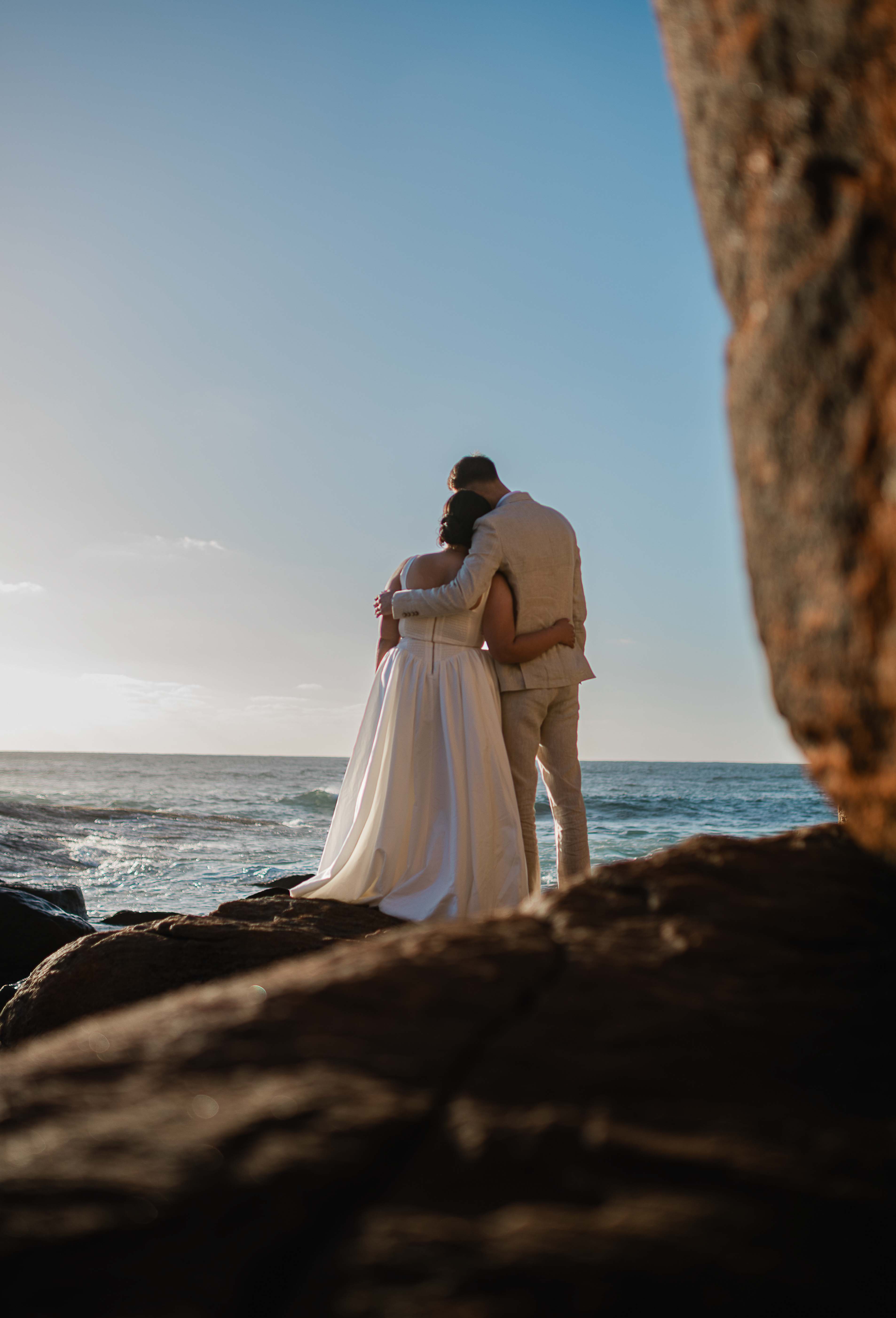 bride and groom cuddle looking out to the golden hour ocean framed by breathtaking cliffs
