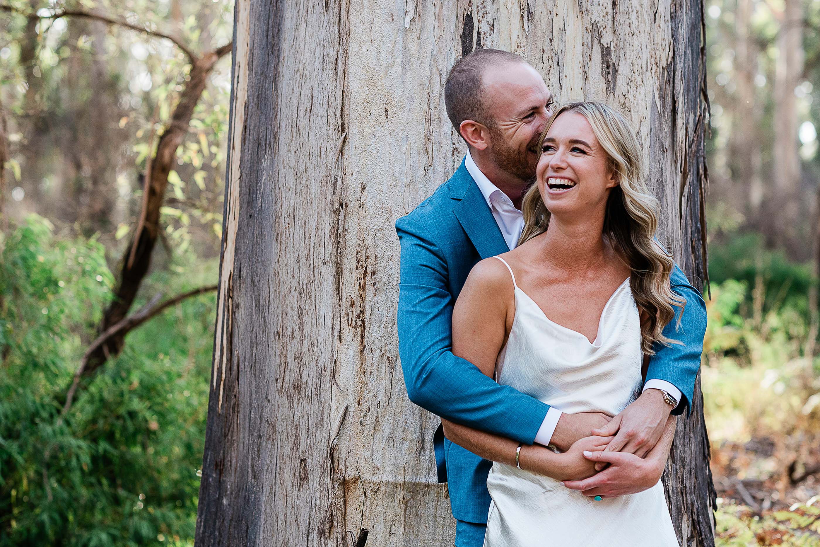 Couple laughing together against a karri tree in Boranup Forest Margaret River elopement portrait by John Rice.